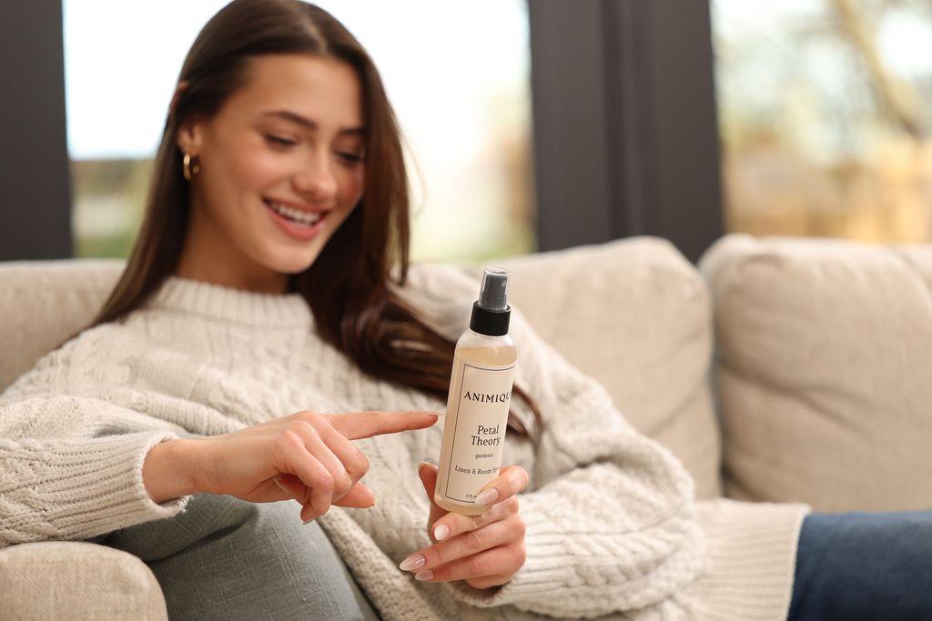Woman sitting on sofa reading label of Animique pet-safe linen and room spray.