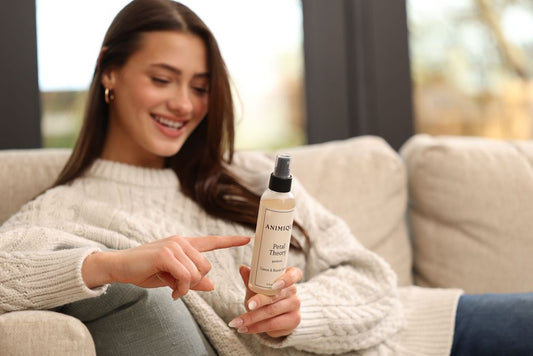 Woman sitting on sofa reading label of Animique pet-safe linen and room spray.