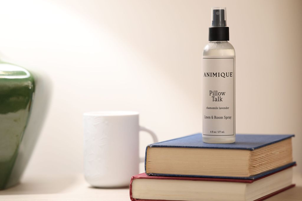 Pillow Talk room and linen spray by Animique — pet-safe home fragrance atop two books on a nightstand next to a cofee mug