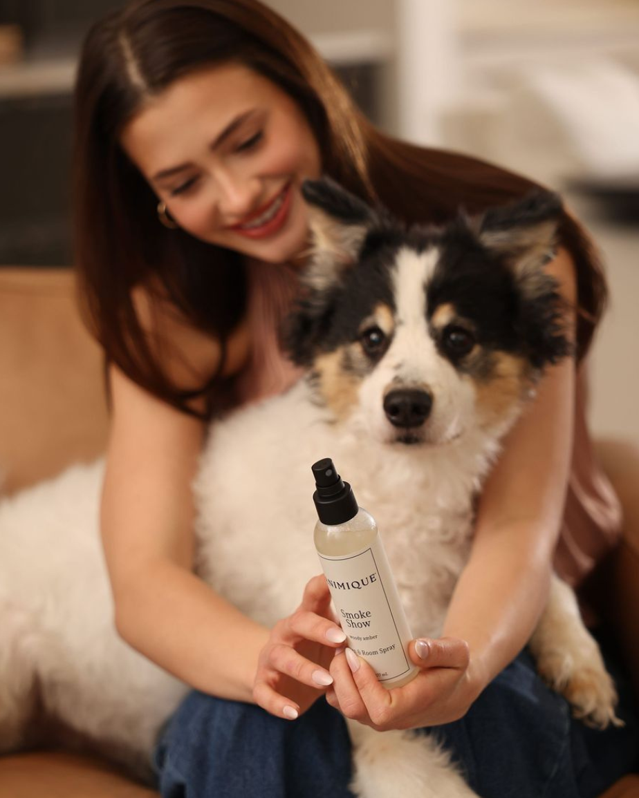 Woman holding a bottle of Smoke Show room and linen spray by Animique - pet safe home fragrance, with a dog sitting on her lap. 